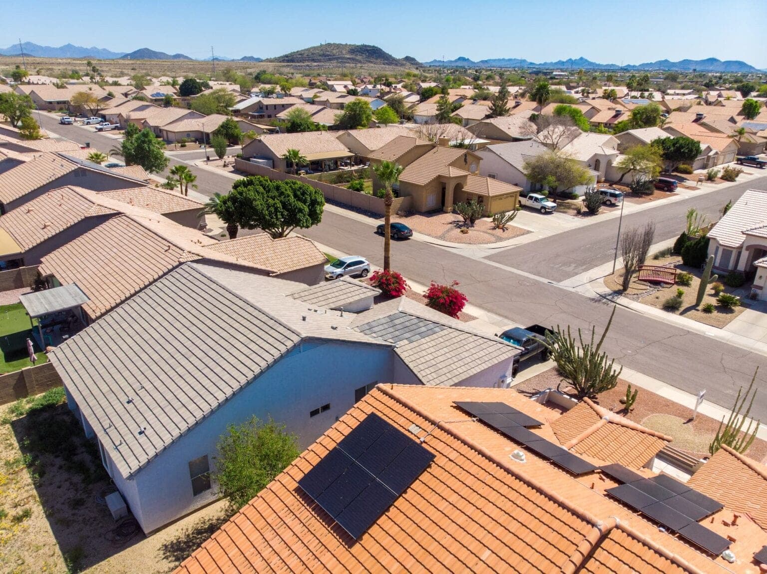 Aerial view of an Arizona neighborhood of tile-roofed homes with rooftop solar panels and desert mountains beyond
