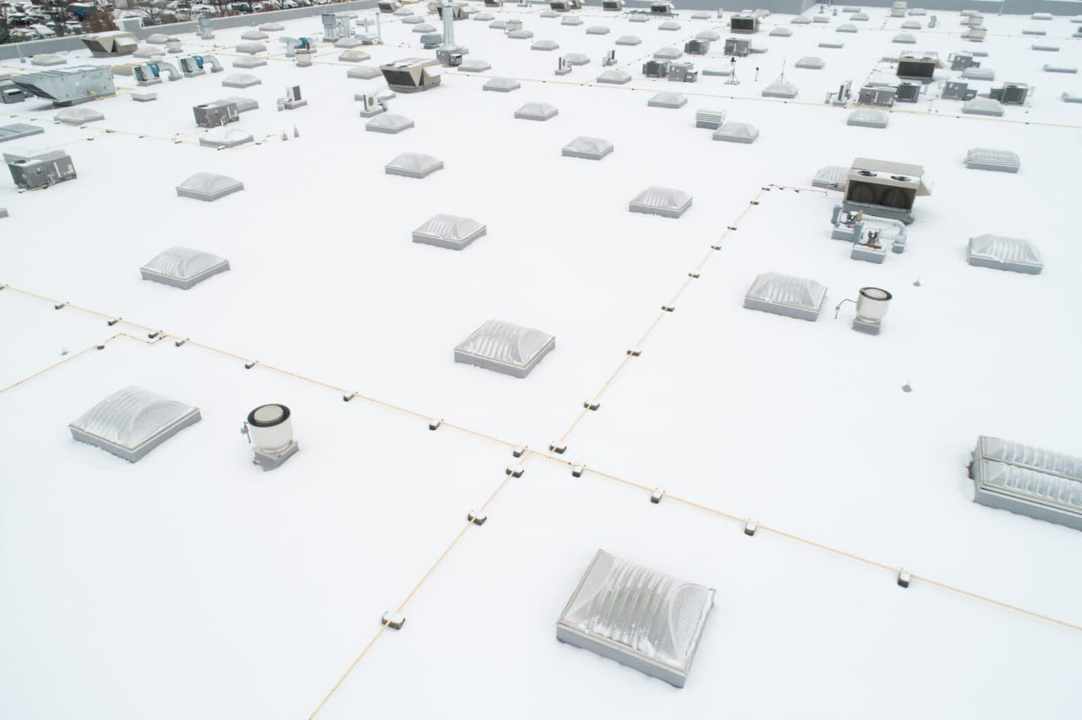 Aerial view of a vast white commercial flat roof covered in skylights and rooftop HVAC units
