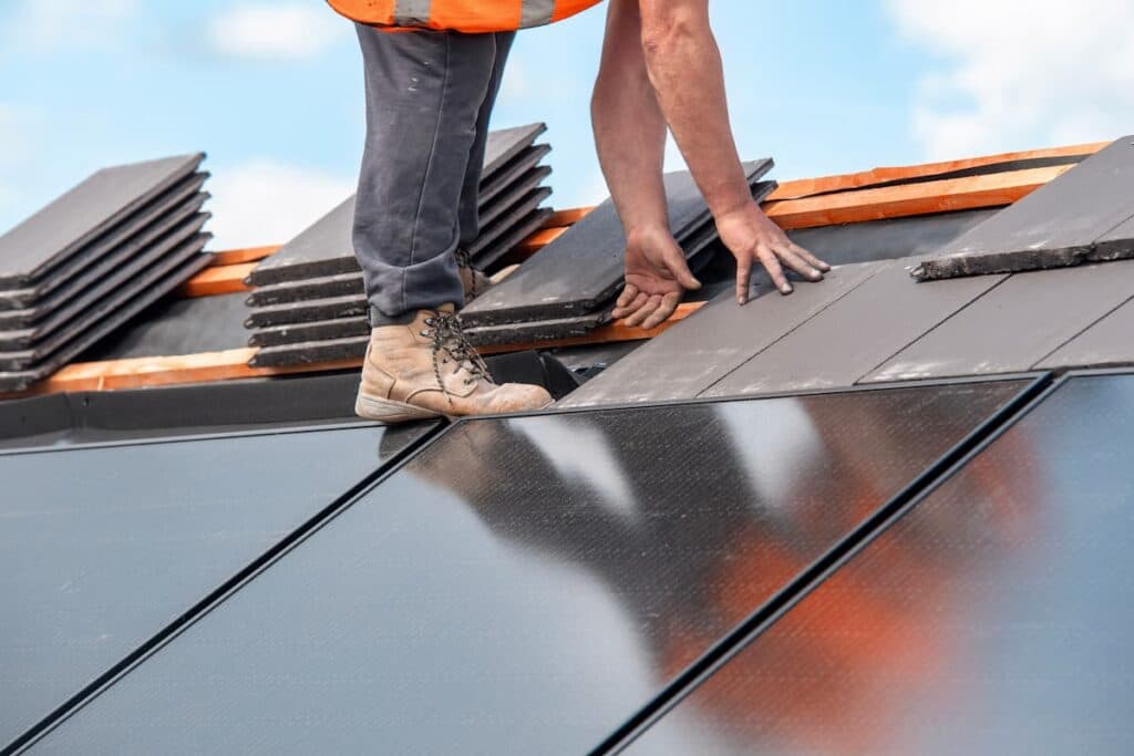 Roofer setting flat roof tiles directly alongside a run of rooftop solar panels
