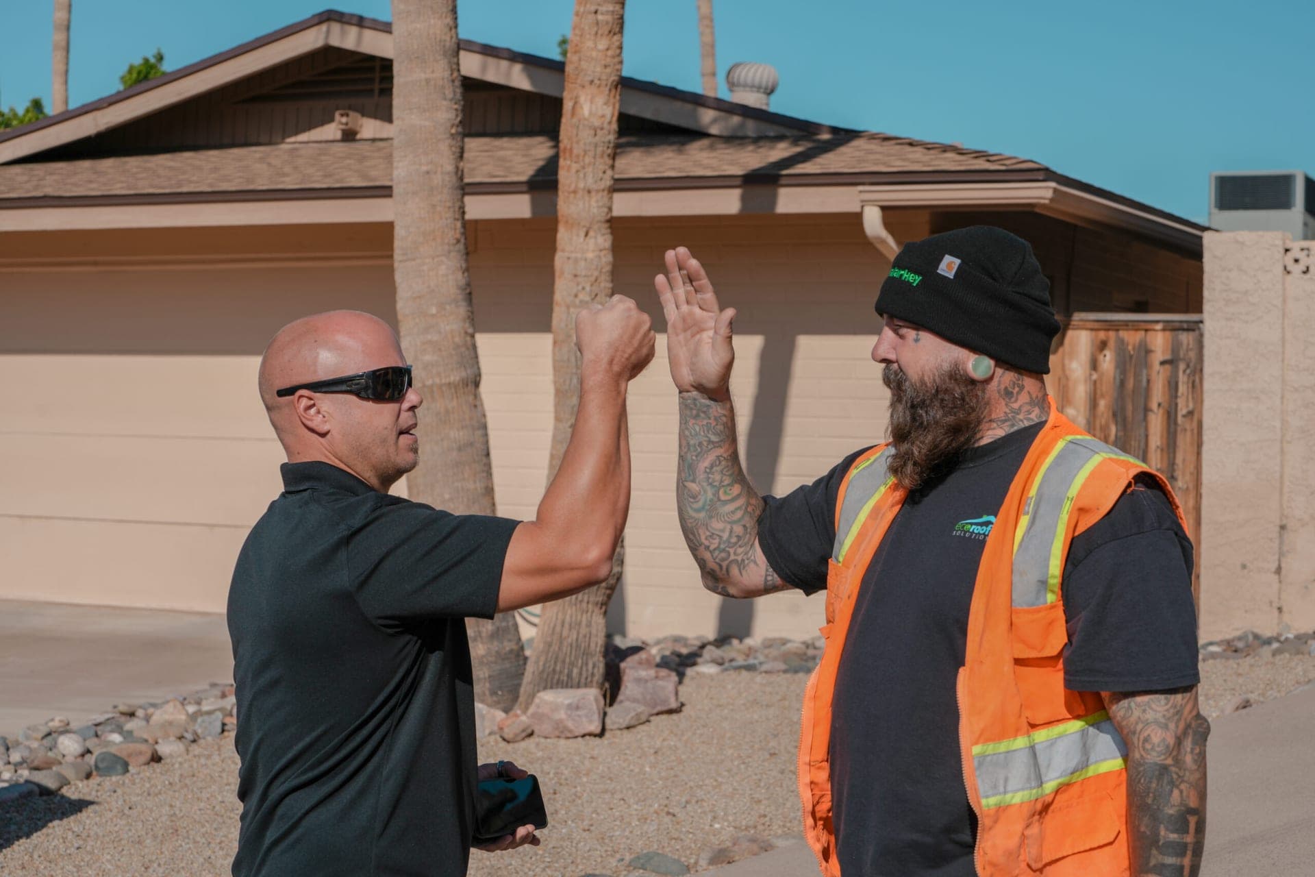 Two Eco Roofing Solutions team members high-fiving in the driveway of an Arizona home after finishing a roof