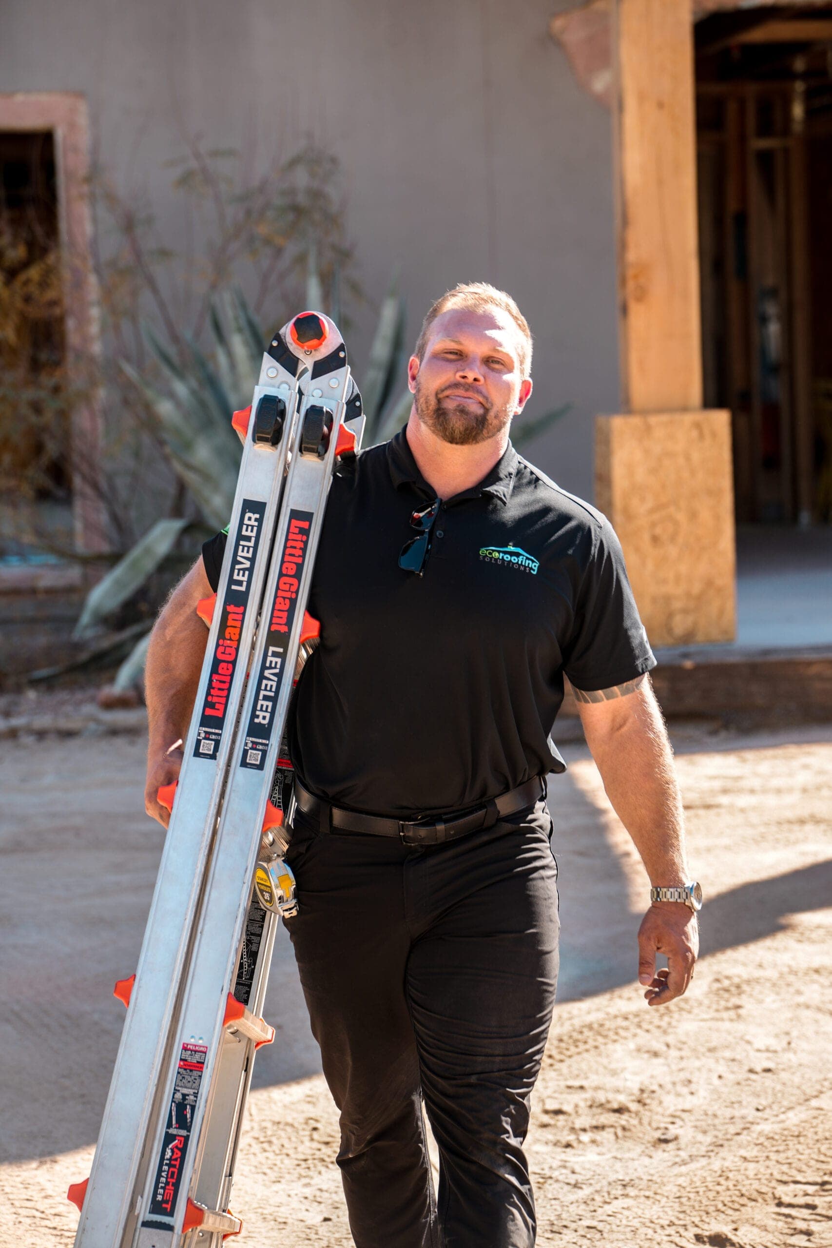 Eco Roofing Solutions team member in a branded polo carrying ladders across a job site