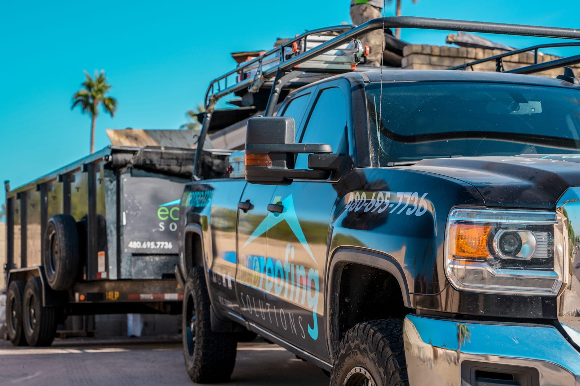 Eco Roofing Solutions branded pickup and dump trailer parked at an Arizona job site with a crew member working on the roof above