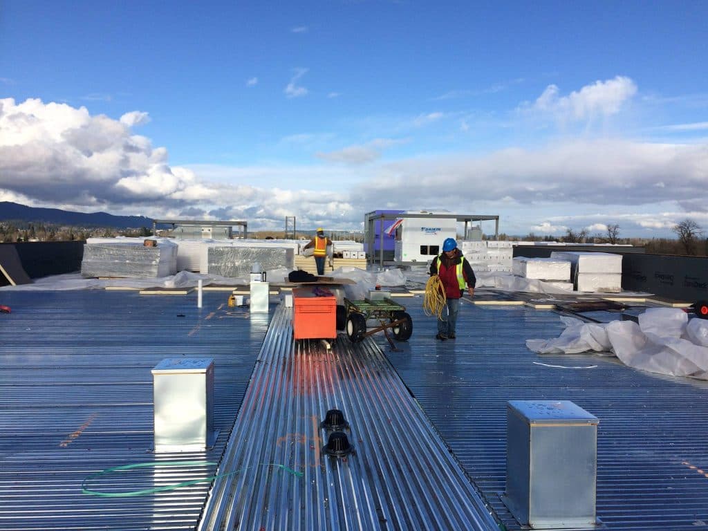 Roofing crew in hard hats staging insulation boards across a steel deck on a large commercial roof
