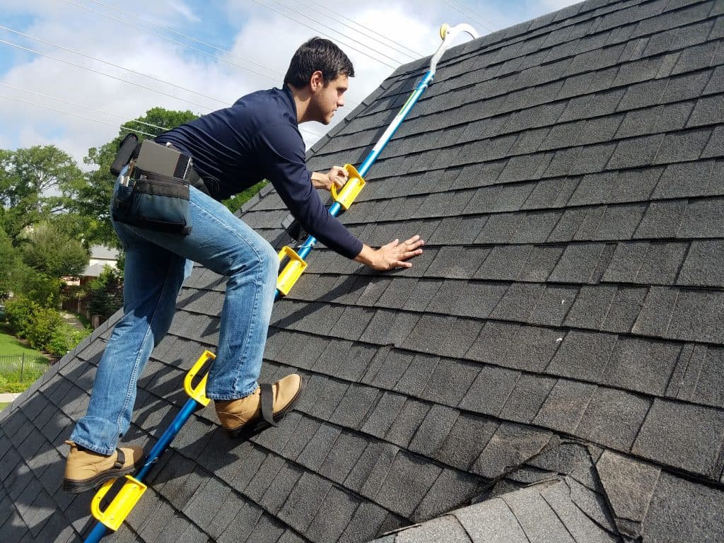 Roofer on roof jacks running a hand across a field of architectural asphalt shingles