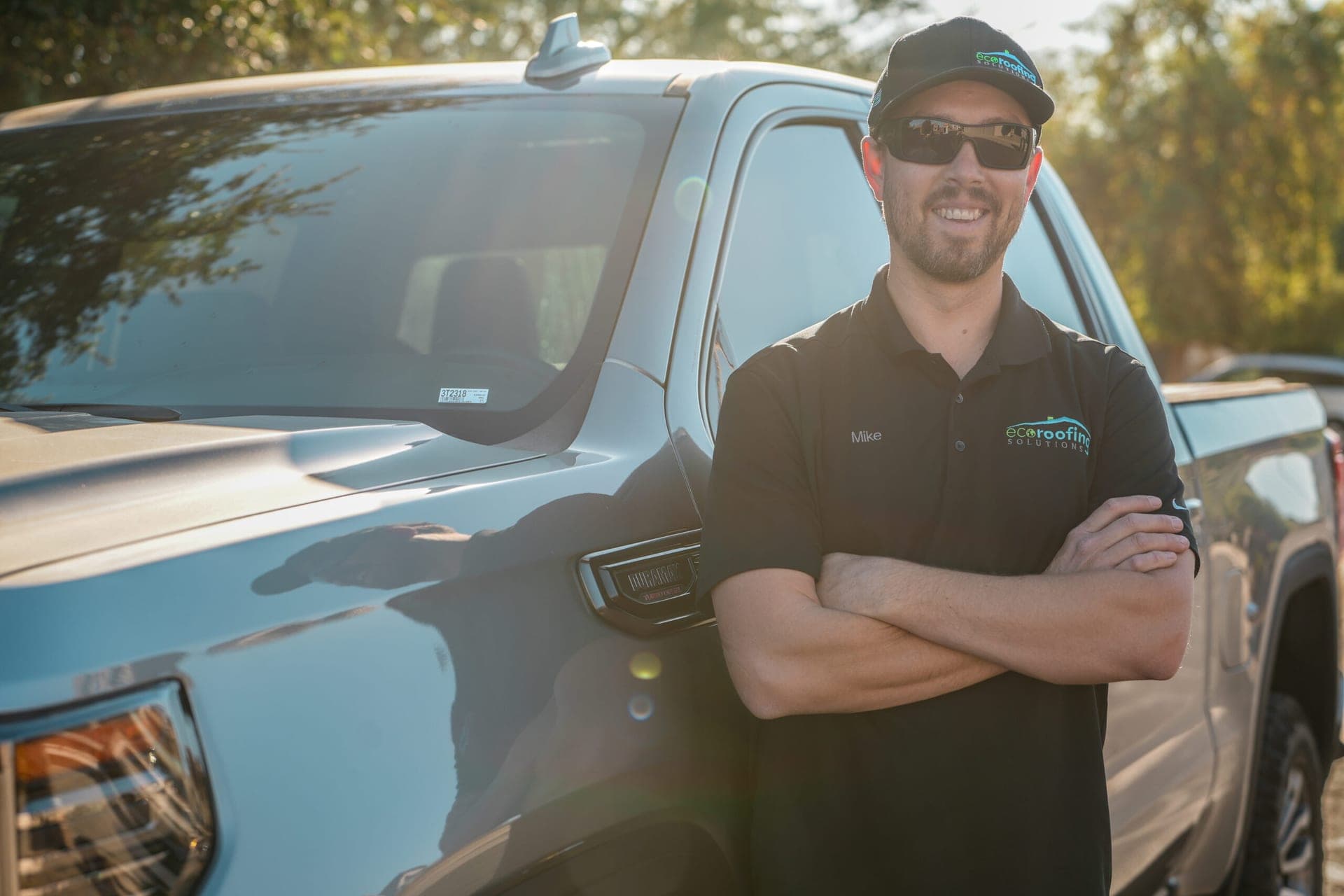 Eco Roofing Solutions team member in a branded polo standing beside a company truck in the late afternoon sun