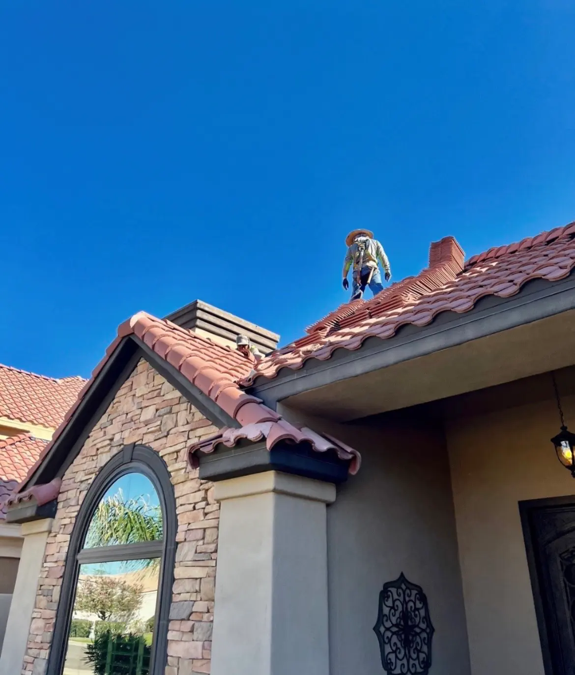 Eco Roofing Solutions crew setting clay barrel tile along the ridge of an Arizona home against a deep blue sky