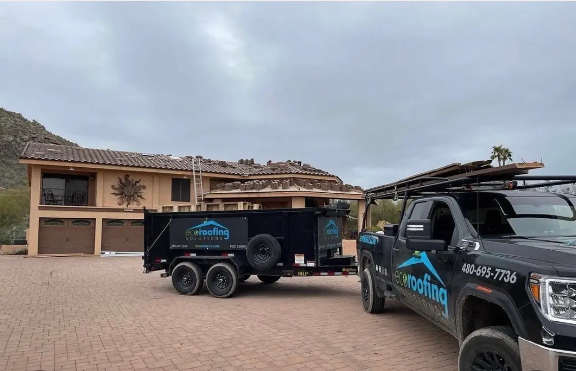 Eco Roofing Solutions branded truck and dump trailer on a paver driveway during a tile roof tear-off at a desert-foothills home