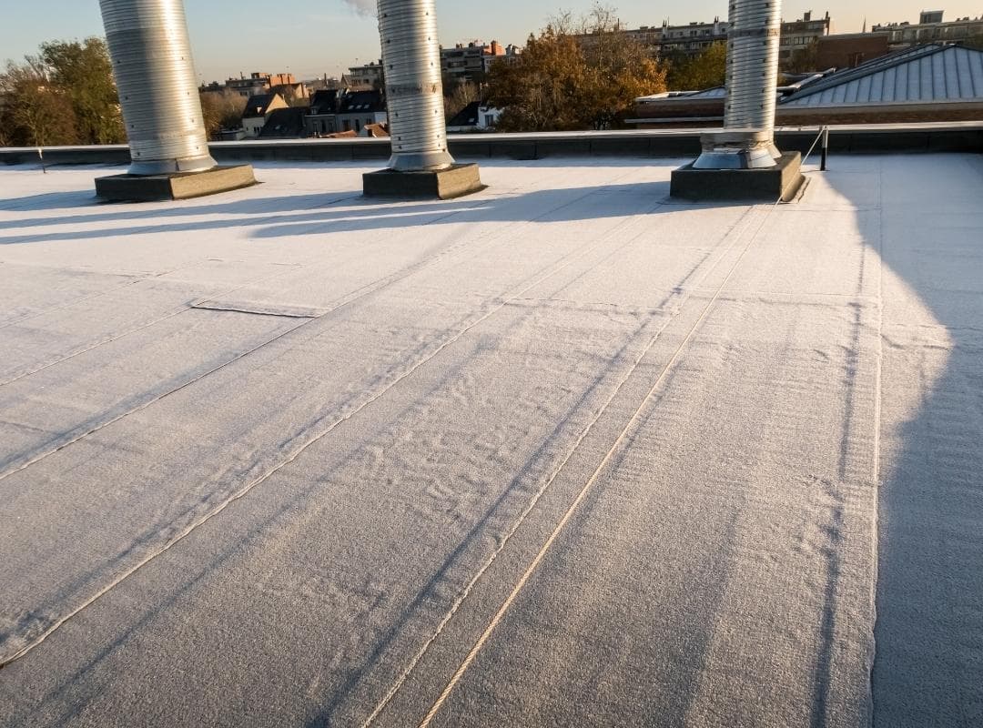 Low-angle view along a single-ply flat roof membrane with sealed seams running past insulated duct penetrations