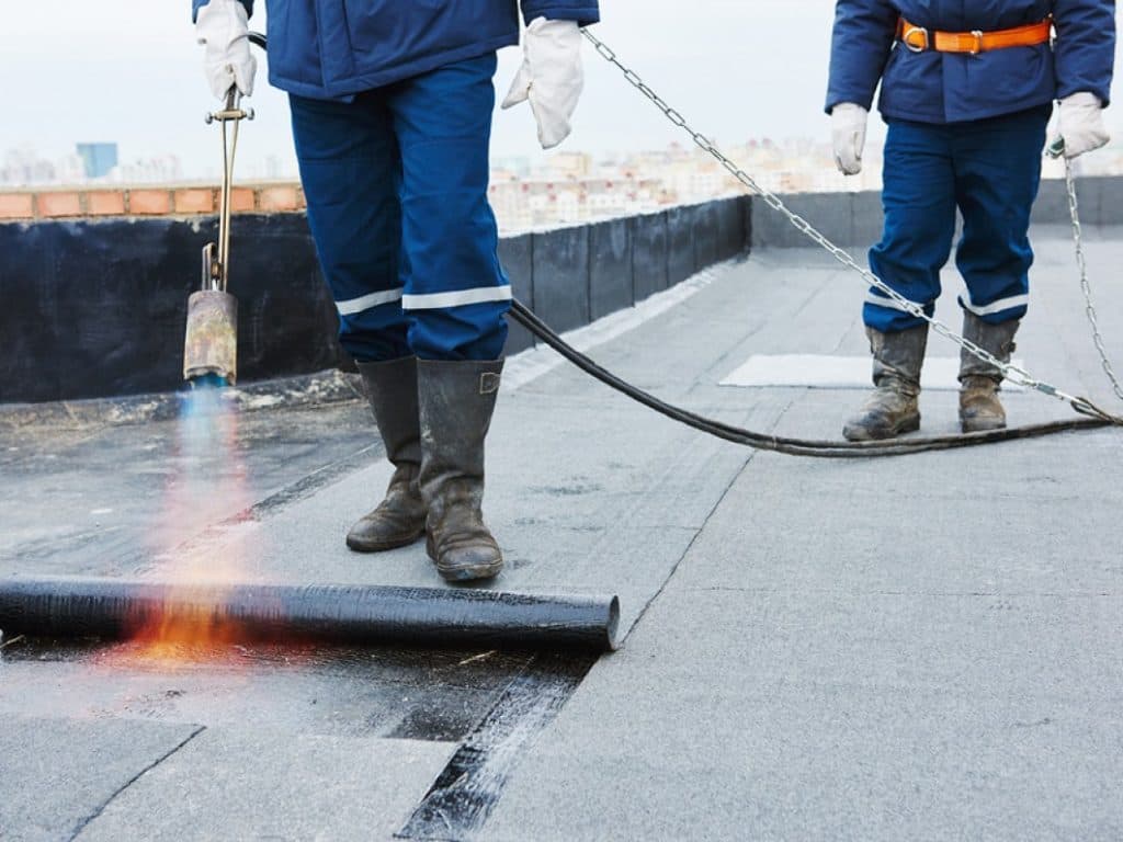 Roofers torch-applying a modified bitumen membrane across a commercial flat roof