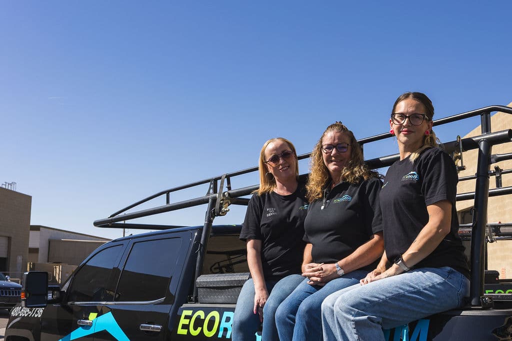 Three Eco Roofing Solutions team members sitting on the ladder rack of a branded truck under a clear Arizona sky
