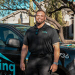 A smiling, bearded man in a black Eco Roofing polo shirt standing in front of a black company truck with "roofing solutions" branding.